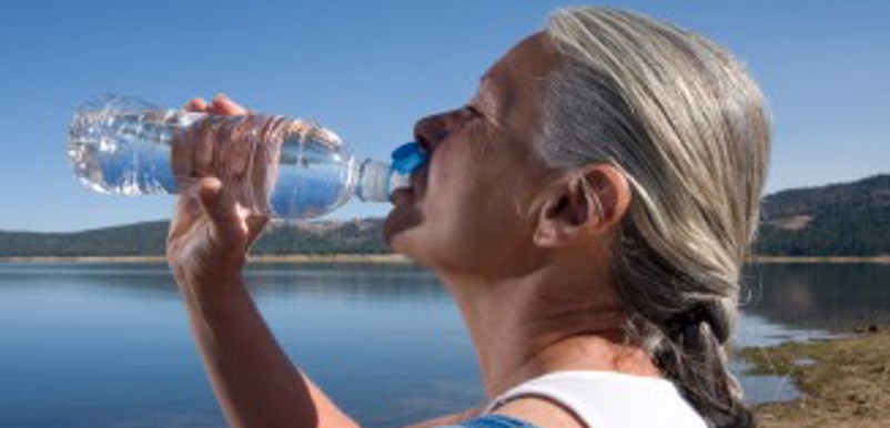 En kvinna vid en sjö dricker vatten ur en plastflaska