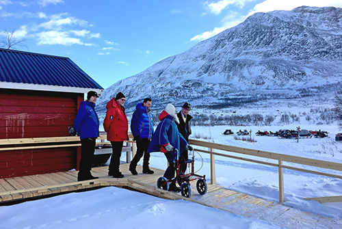 En fjällstuga med ramp där det står fem personer varav en med rullator