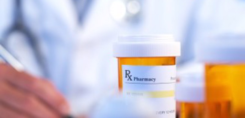 Närbild på en medicinburk med tabletter, en läkare i bakgrunden