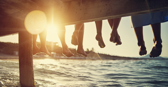 Fem personers fötter hänger ner från en brygga vid en sjö
